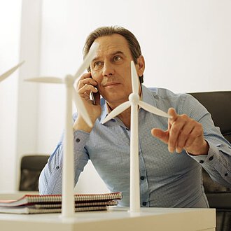 Mann mit Telefon am Ohr sitzt an Tisch mit Windenergieanlagen-Modell
